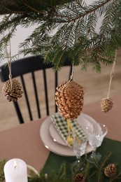 Christmas celebration. Cones hanging from fir tree branch over table with burning candle and tableware