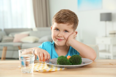 Photo of Adorable little boy with plate of vegetables at table in living room