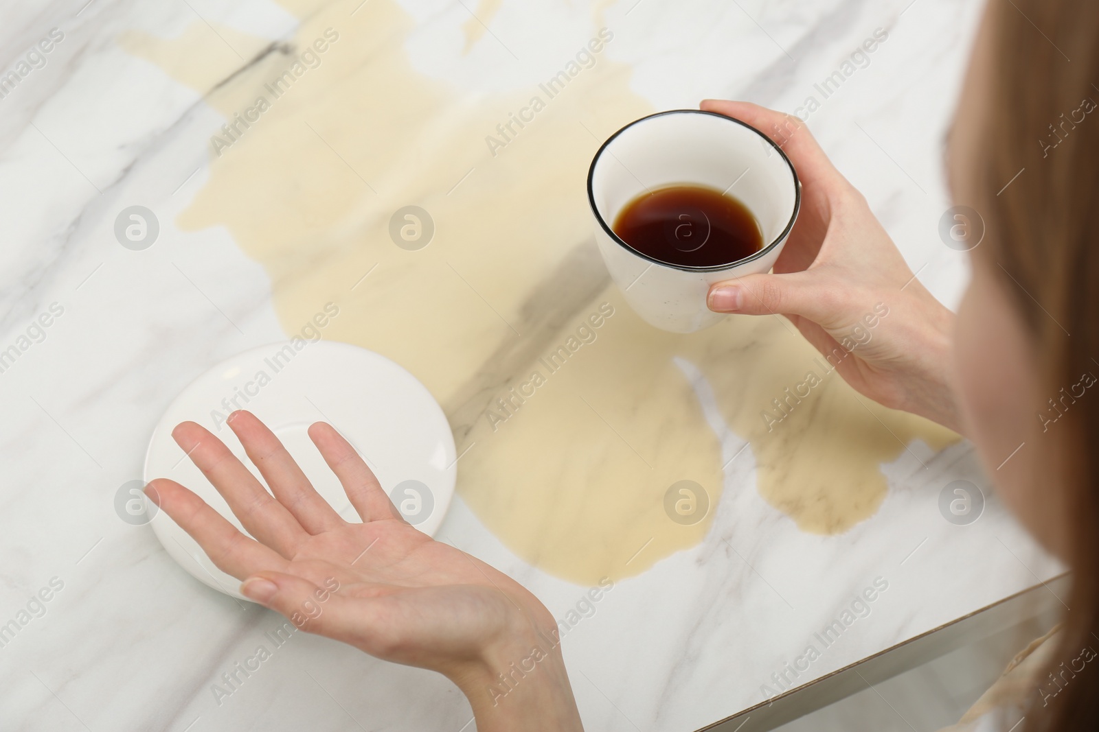 Photo of Woman holding cup near spot of coffee at marble table, closeup