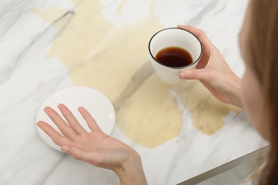 Woman holding cup near spot of coffee at marble table, closeup