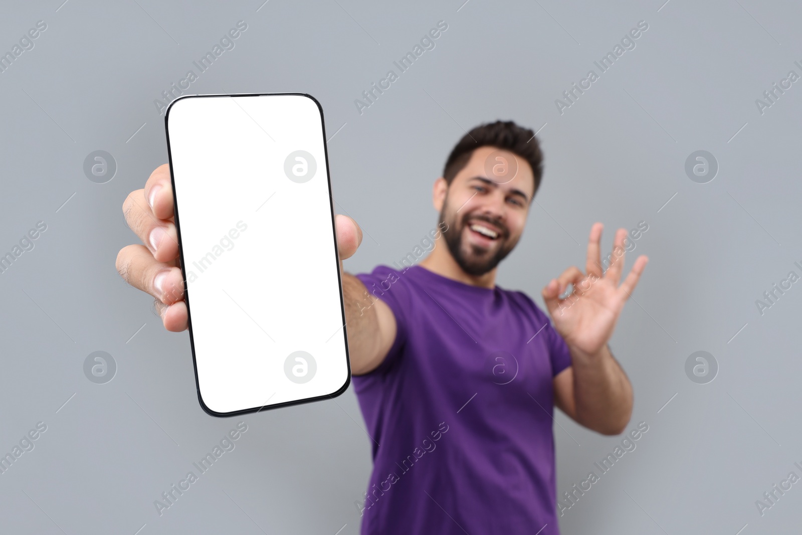 Photo of Young man showing smartphone in hand and OK gesture on light grey background, selective focus. Mockup for design