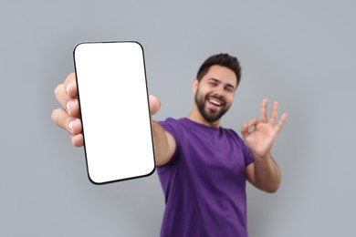 Young man showing smartphone in hand and OK gesture on light grey background, selective focus. Mockup for design