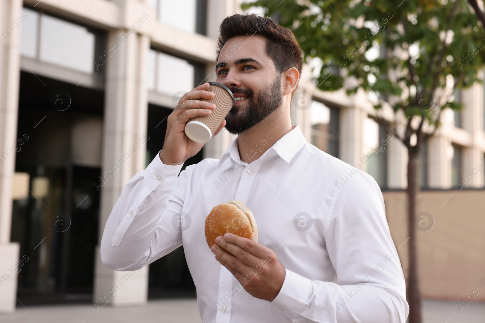 Photo of Businessman with hamburger and paper cup of coffee having lunch outdoors