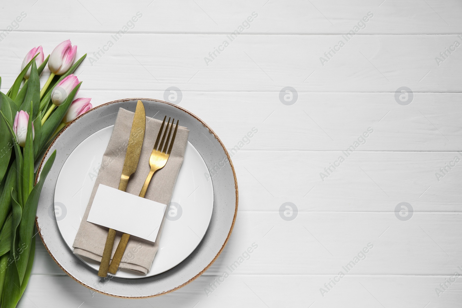 Photo of Stylish table setting with cutlery, paper card and tulips on white wooden background, flat lay. Space for text