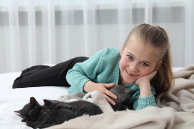 Photo of Little girl with cute fluffy kittens on bed indoors