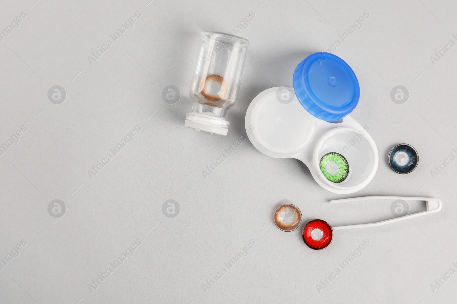 Photo of Different color contact lenses, tweezers and containers on light background, flat lay. Space for text