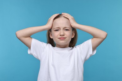 Little girl suffering from headache on light blue background