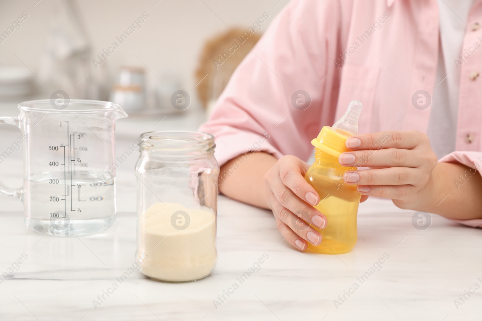 Photo of Woman preparing infant formula at table indoors, closeup. Baby milk