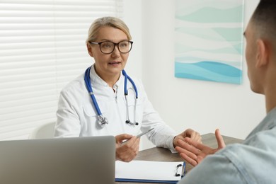 Photo of Professional doctor consulting patient at wooden table in clinic