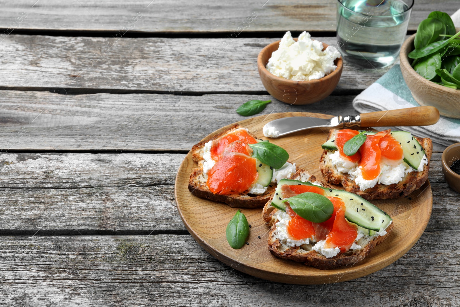 Photo of Delicious sandwiches with cream cheese, salmon, cucumber and spinach on wooden table. Space for text