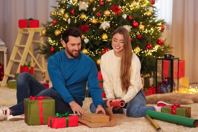 Happy couple decorating Christmas gift with wrapping paper at home
