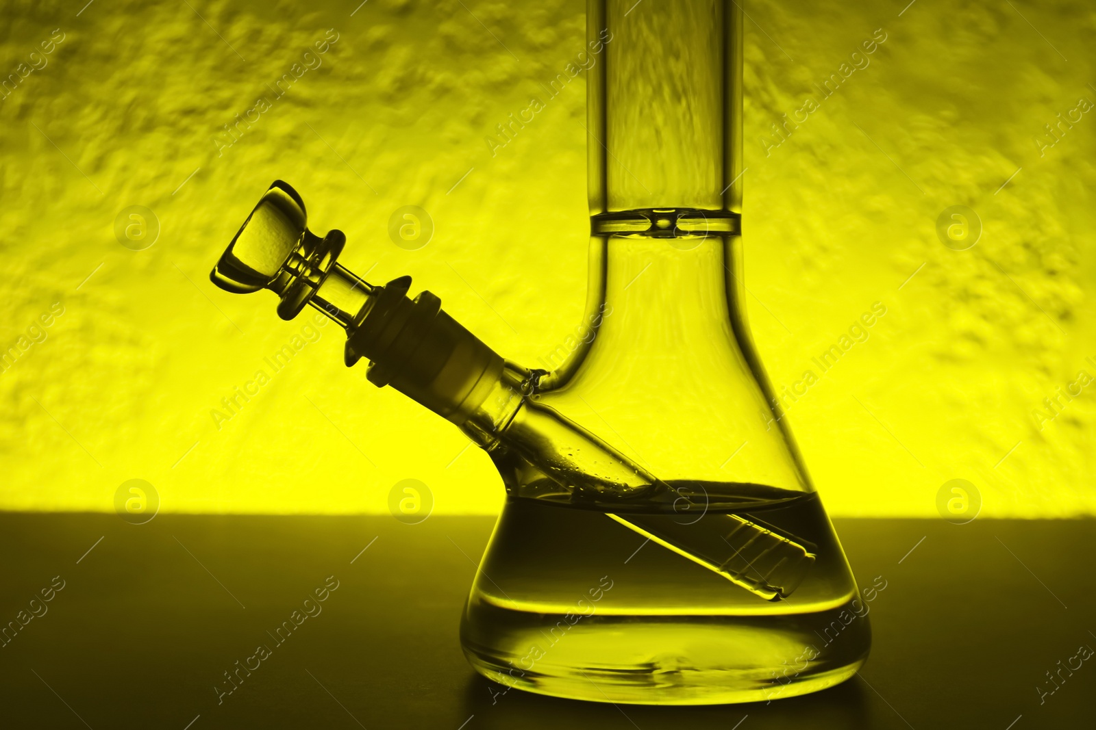 Photo of Closeup view of glass bong on table, toned in yellow. Smoking device