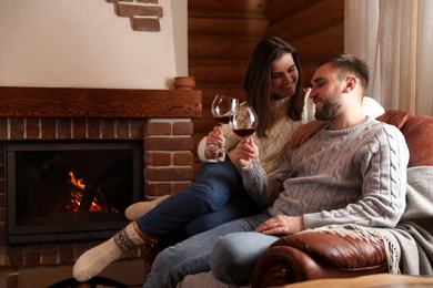 Lovely couple with glasses of wine resting near fireplace at home. Winter vacation