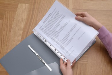 Woman putting punched pocket with document into file folder at wooden table, above view