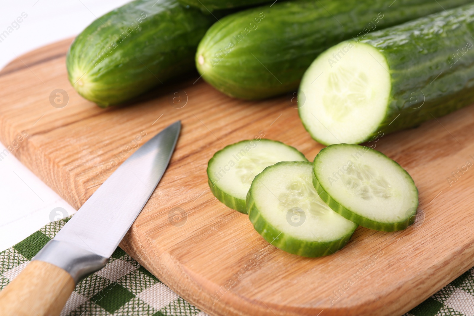 Photo of Fresh cucumbers and knife on wooden cutting board, closeup