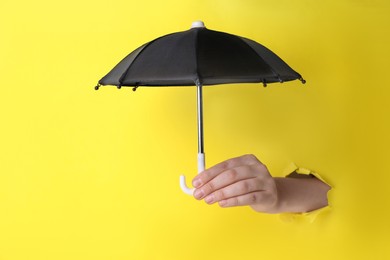 Photo of Woman holding open small black umbrella through hole in yellow paper, closeup