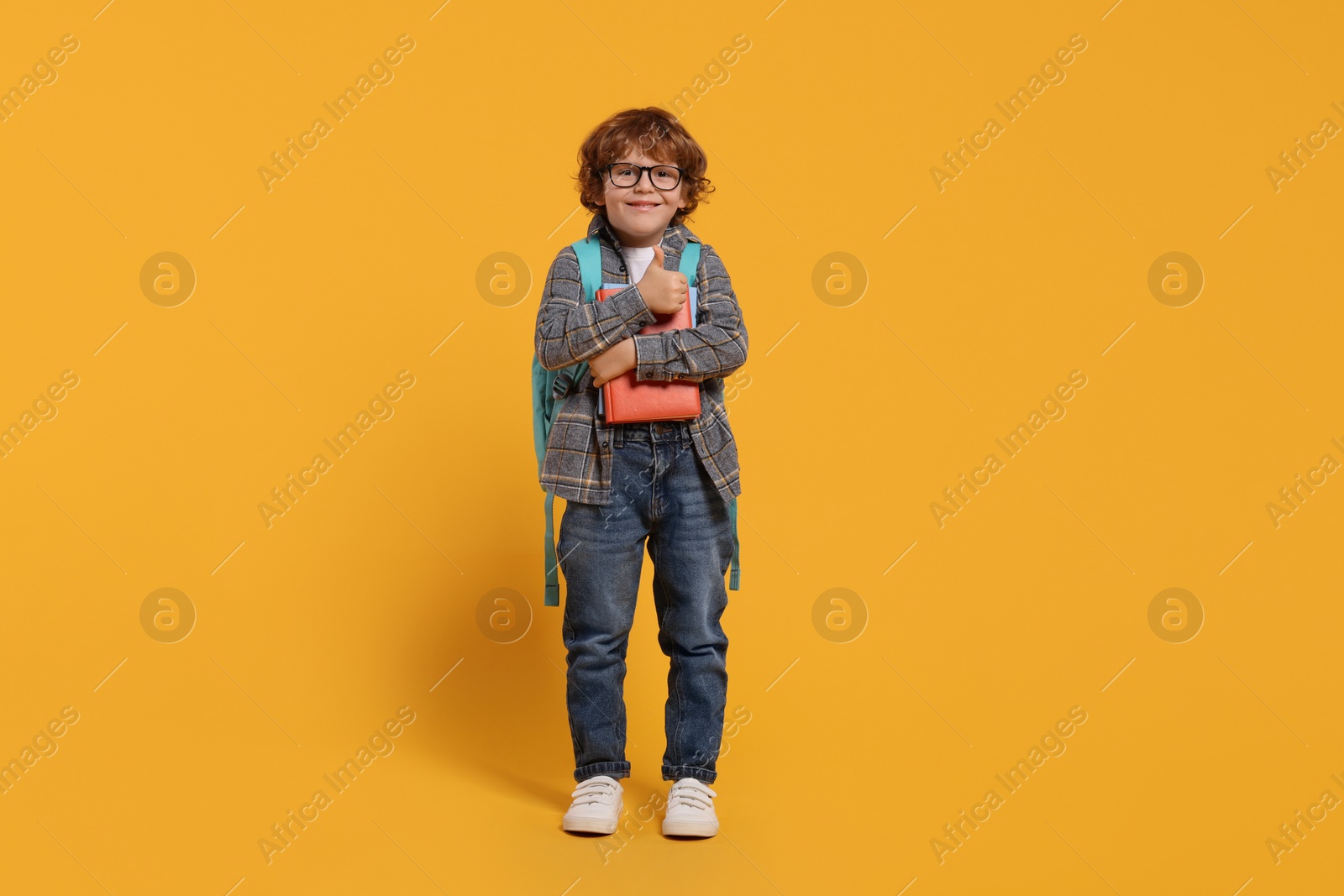 Photo of Happy schoolboy with backpack and books on orange background