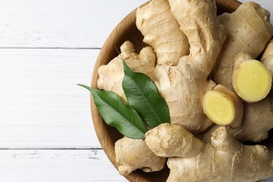 Fresh ginger with leaves in bowl on white wooden table, top view