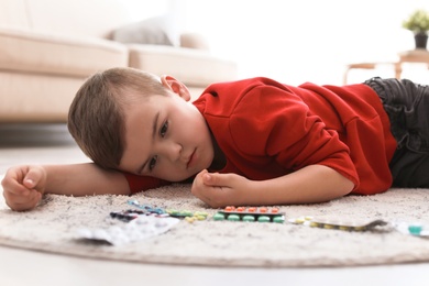 Little child with pills lying on floor at home. Household danger