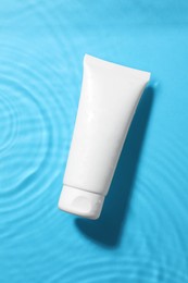 Tube with moisturizing cream in water on light blue background, top view