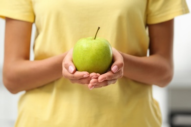 Woman holding fresh green apple indoors, closeup