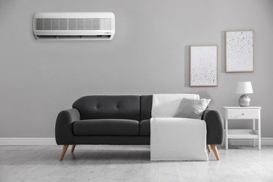 Modern air conditioner on light grey wall in room with stylish sofa