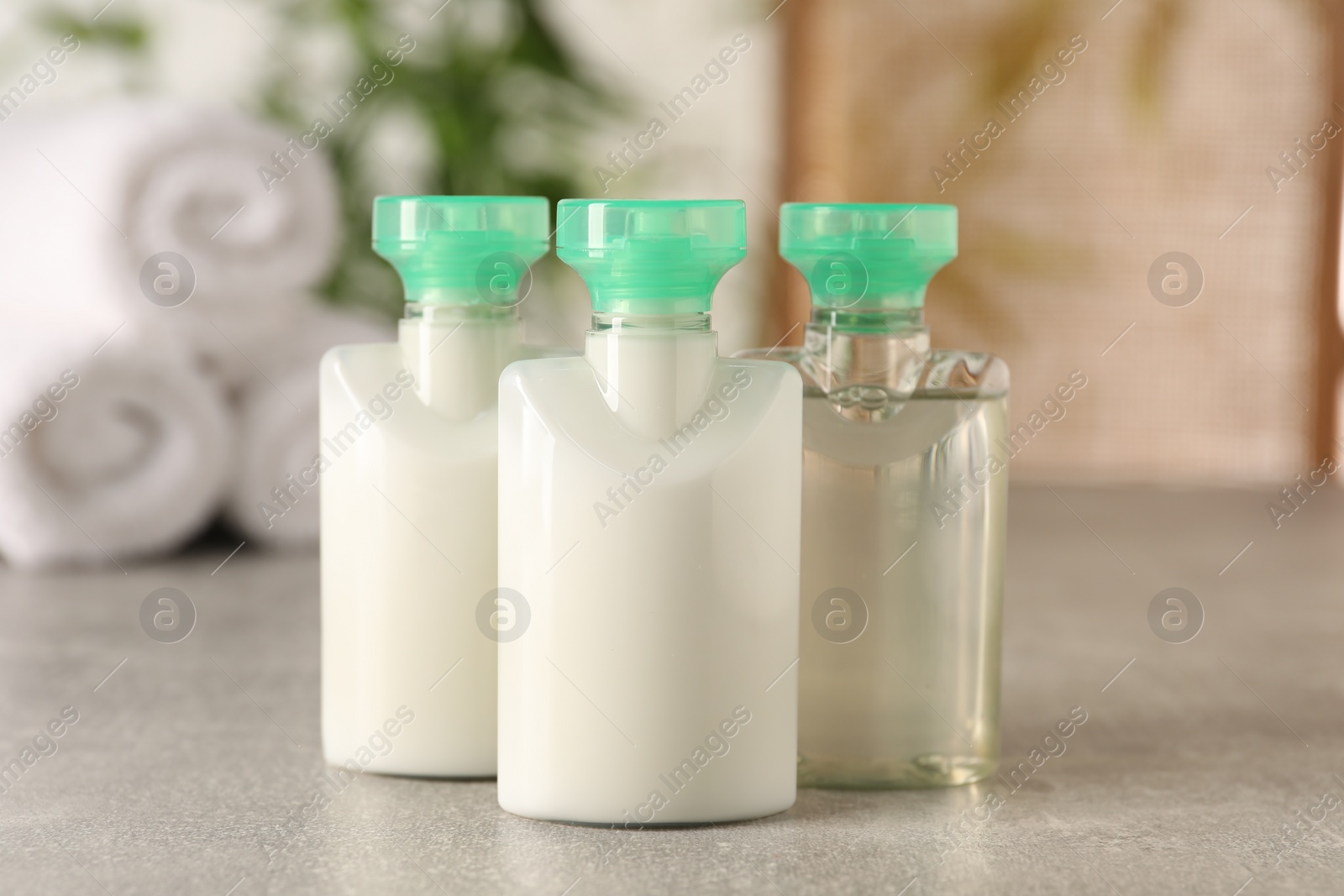 Photo of Mini bottles of cosmetic products on light grey table against blurred background, closeup