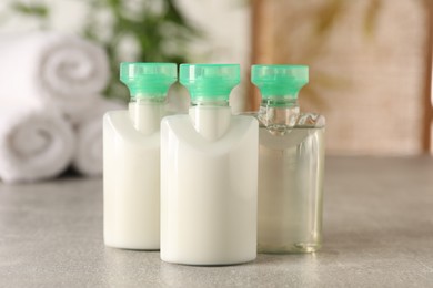 Photo of Mini bottles of cosmetic products on light grey table against blurred background, closeup