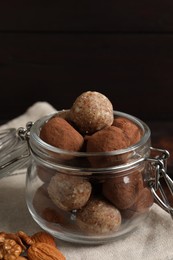 Photo of Different delicious vegan candy balls in glass jar and nuts on table