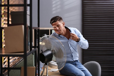 Photo of Man enjoying air flow from fan at workplace