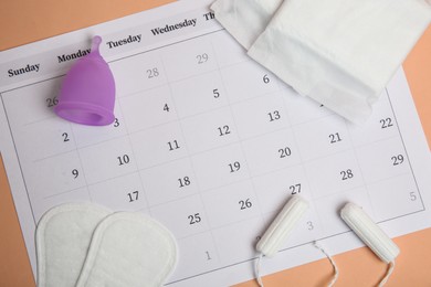 Photo of Flat lay composition with calendar and menstrual pads on pale orange background