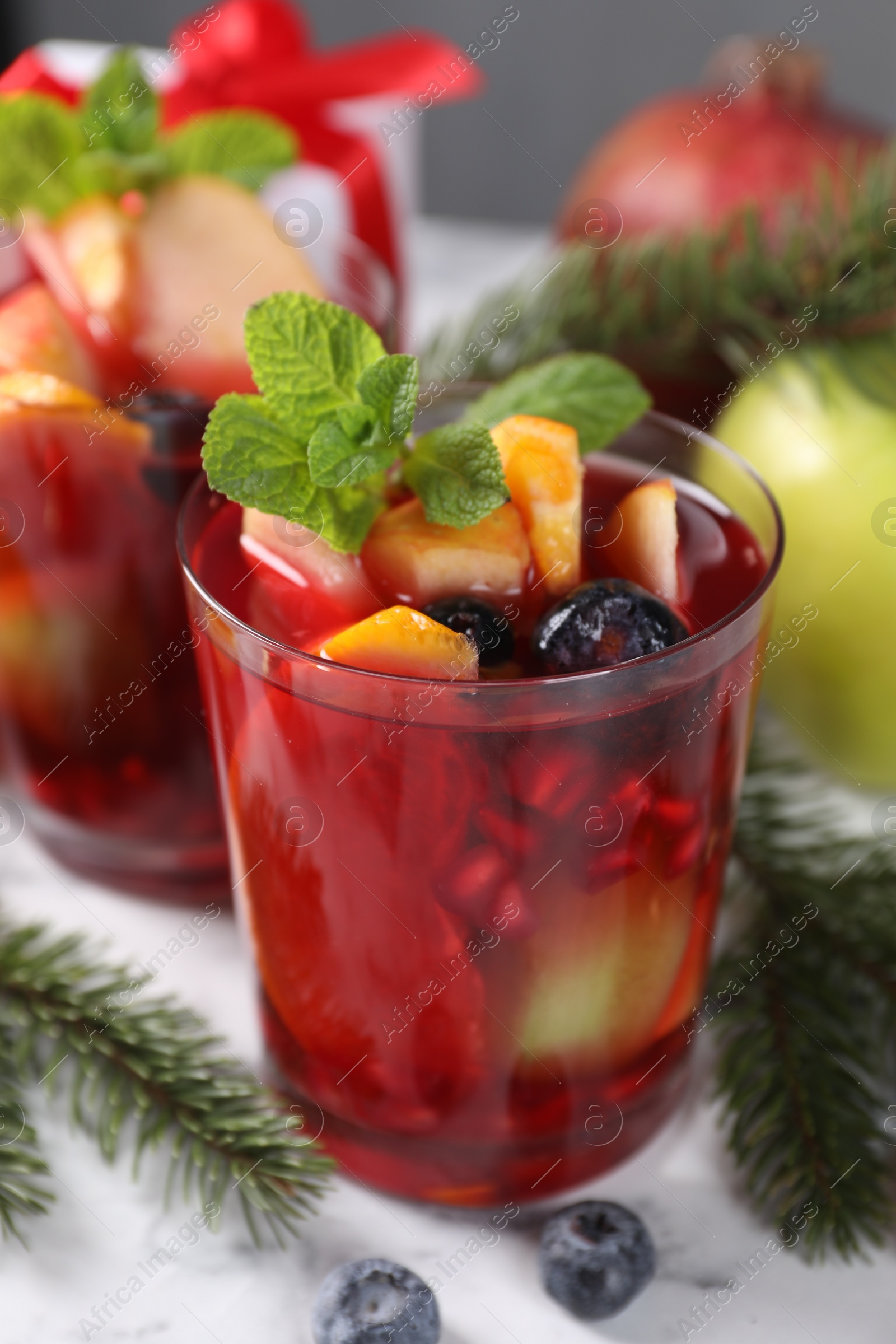 Photo of Aromatic Sangria drink in glasses, ingredients and Christmas decor on white marble table