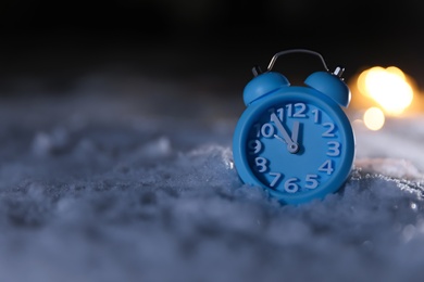 Photo of Alarm clock and Christmas lights on white snow outdoors, space for text. Midnight countdown