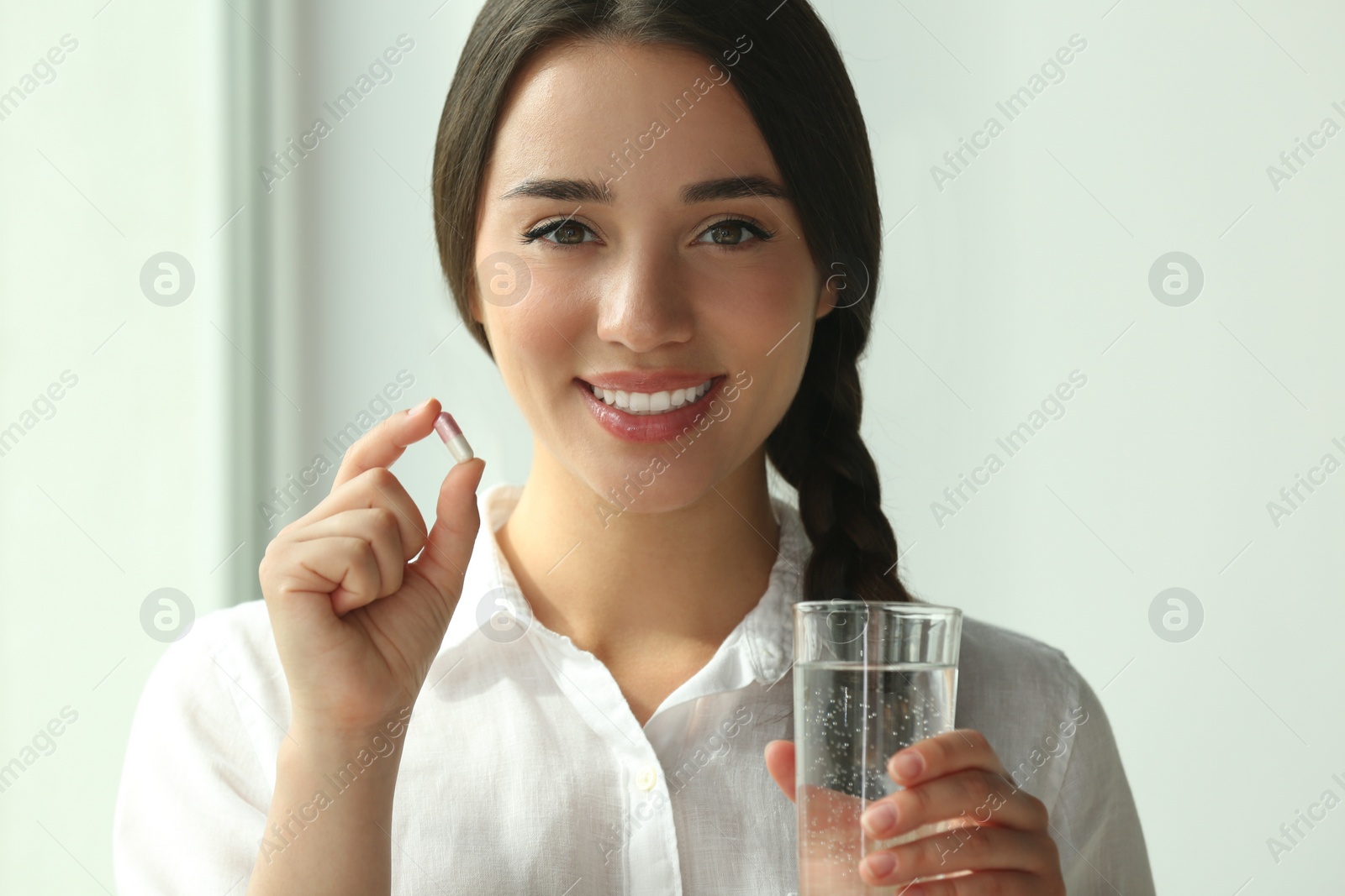 Photo of Young woman with glass of water and dietary supplement pill indoors