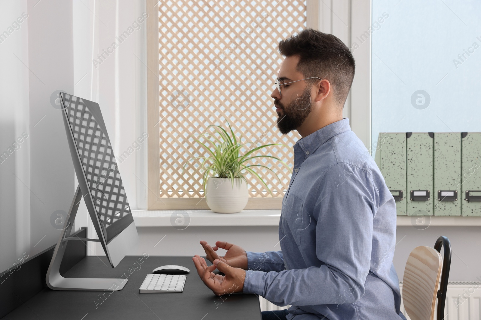 Photo of Young businessman meditating at workplace. Zen concept