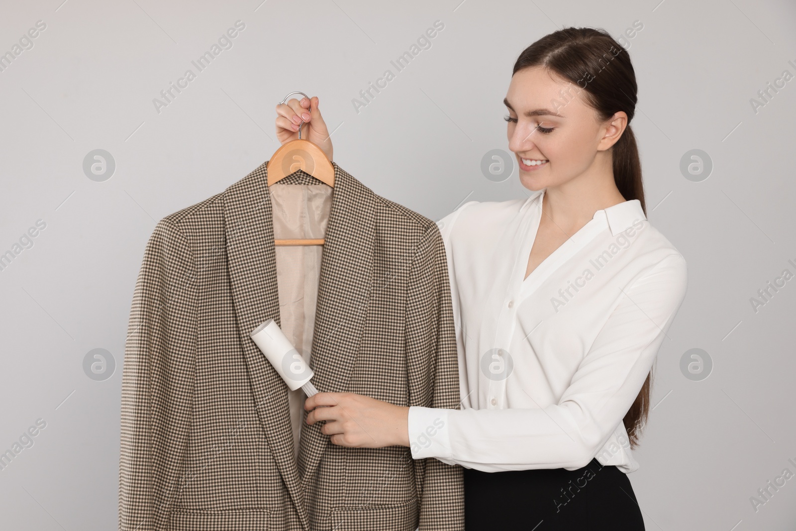 Photo of Young woman using adhesive lint roller on light grey background. Dry-cleaning service