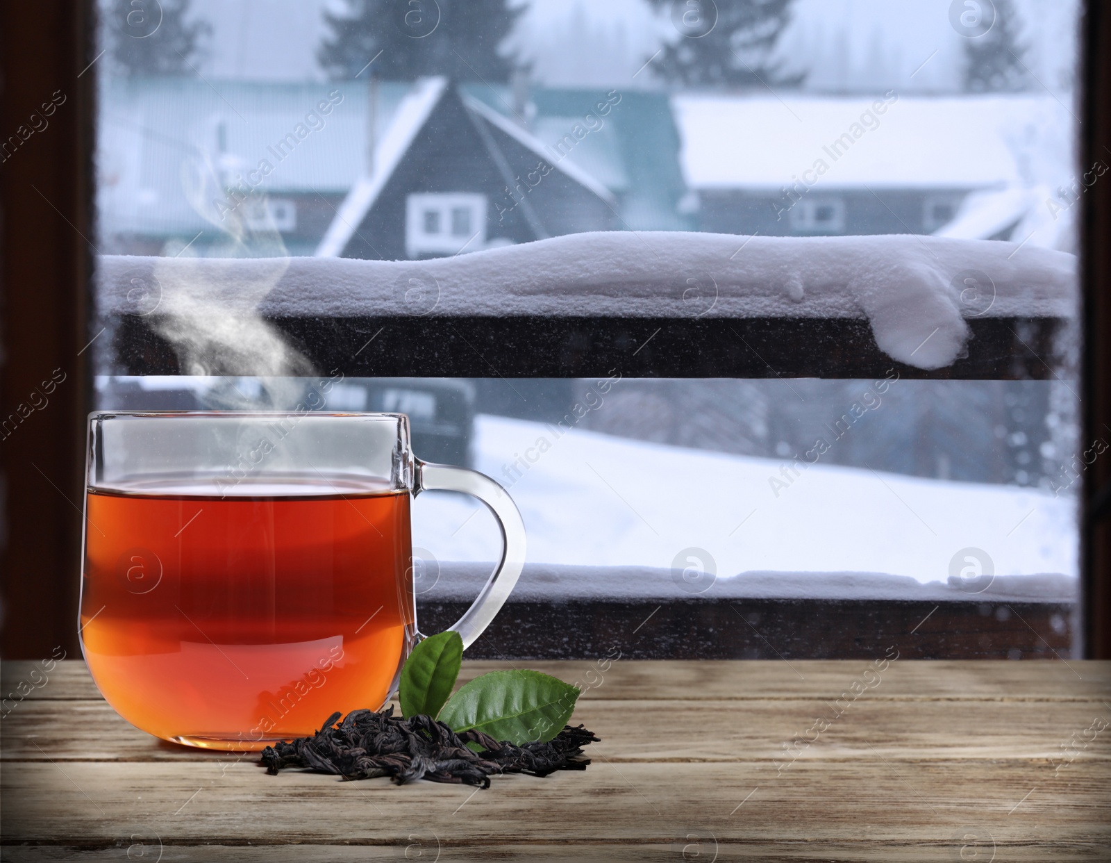 Image of Cup of hot tea on wooden table near window covered with frost 