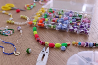 Photo of Beautiful handmade beaded jewelry and supplies on wooden table, closeup