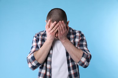 Photo of Upset man closing his face with hands on light blue background