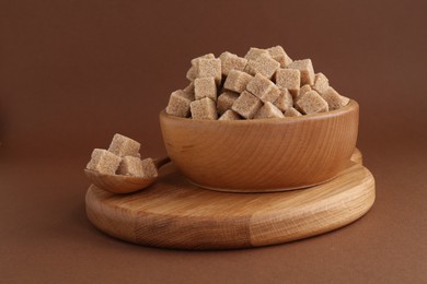 Photo of Brown sugar cubes in bowl and spoon on color background