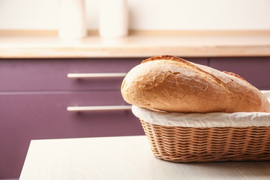 Photo of Wicker basket with loaf of tasty fresh bread on wooden table in kitchen