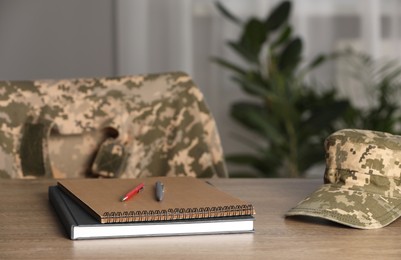 Photo of Notebooks, soldier cap and pens on wooden table indoors. Military education