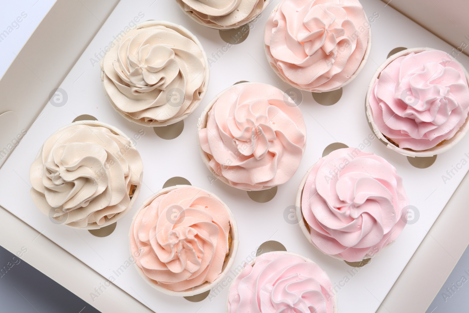 Photo of Many tasty cupcakes with colorful cream in box, top view