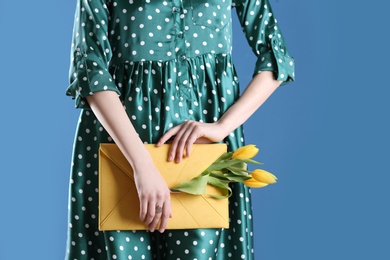 Photo of Woman holding elegant clutch with spring flowers on blue background, closeup. Space for text