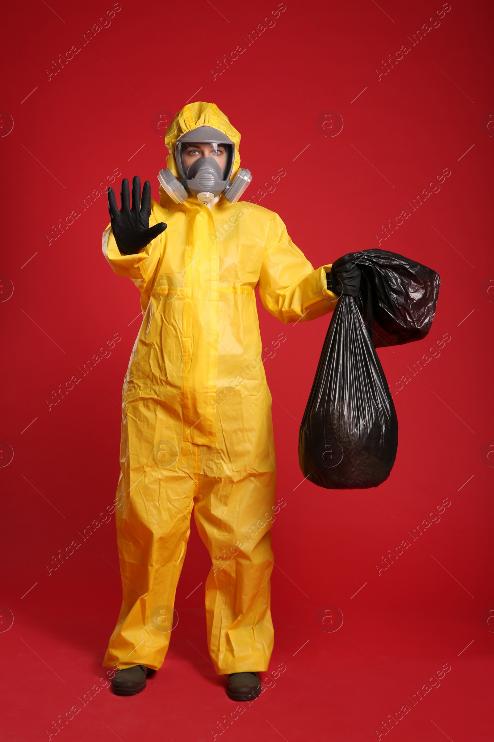 Photo of Woman in chemical protective suit holding trash bag on red background. Virus research