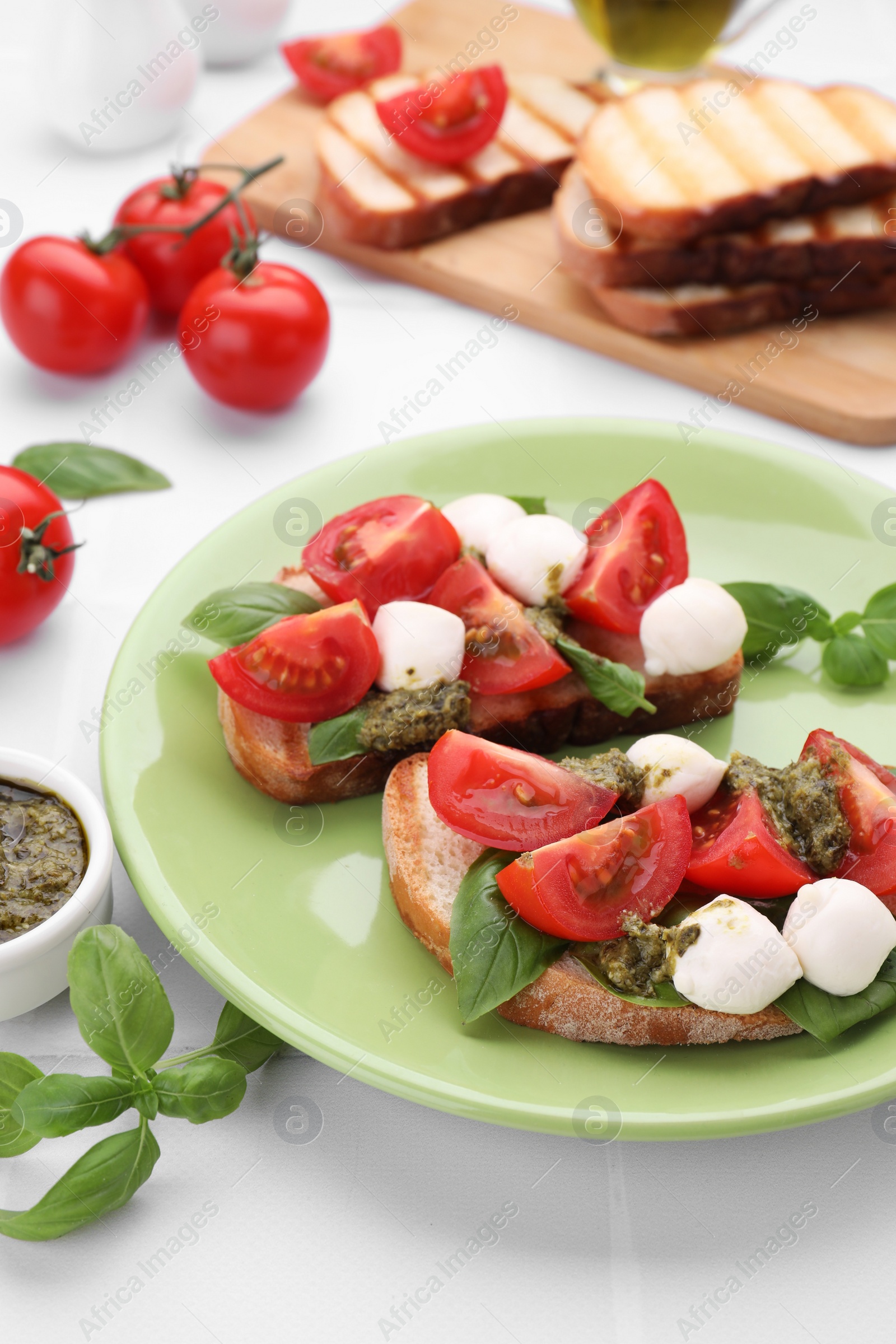 Photo of Delicious Caprese sandwiches with mozzarella, tomatoes, basil and pesto sauce on white tiled table