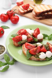 Photo of Delicious Caprese sandwiches with mozzarella, tomatoes, basil and pesto sauce on white tiled table