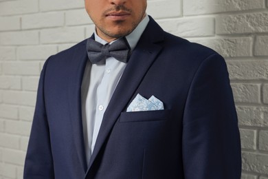 Photo of Man with handkerchief in breast pocket of his suit near white brick wall, closeup