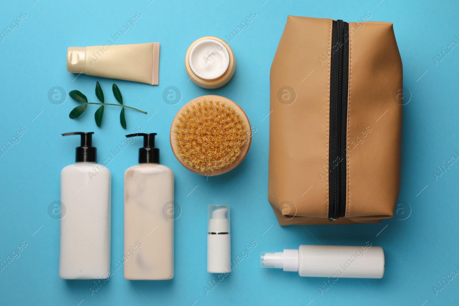 Photo of Preparation for spa. Compact toiletry bag and different cosmetic products on light blue background, flat lay