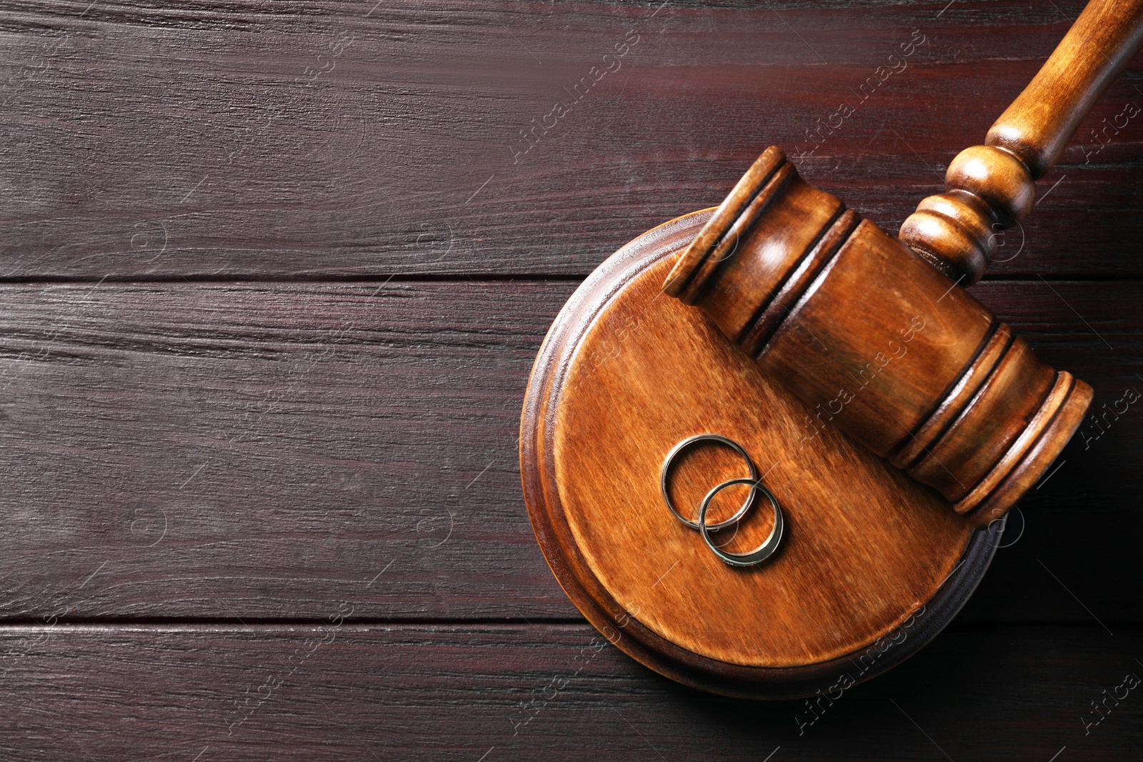 Photo of Divorce concept. Gavel and wedding rings on black wooden table, top view with space for text